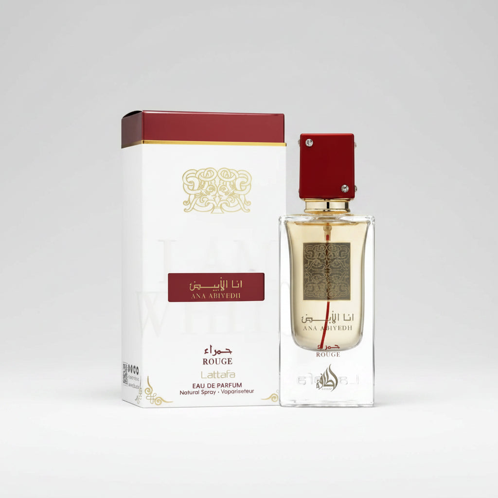 A bottle of Ana abiyedh rouge Eau de Parfum next to its white and red packaging box, featuring gold Arabic calligraphy and a red cap, on a white background.