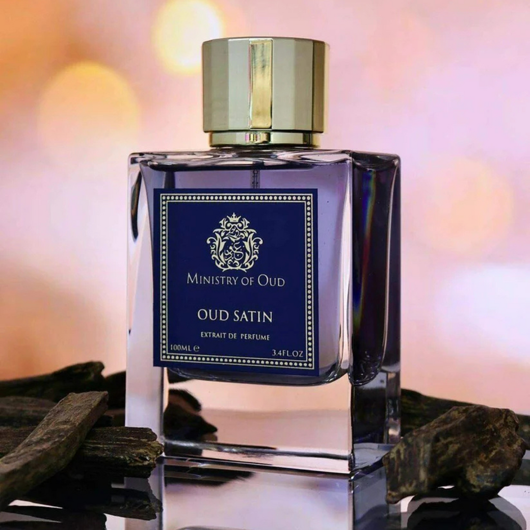 Paris Corner Oud Satin EDP 100ml perfume bottle slight side angle on mirrored table with wood pieces and rose orange background – opulent sweet floral oud scent with violet rose bergamot, Turkish rose oud benzoin, vanilla amber musk
