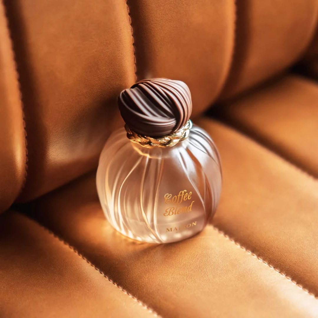Maison Asrar Coffee Blend EDP 100ml perfume bottle top view resting on beige leather car seat – luxurious coffee gourmand fragrance with coffee bergamot, caramel vanilla jasmine, amber tonka bean sandalwood musk