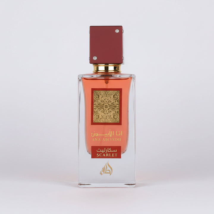 A rectangular glass perfume bottle with amber-orange liquid, a gold patterned label, and a dark red cap, shown on a plain white background. The label includes Arabic text and the word 'SCARLET'.