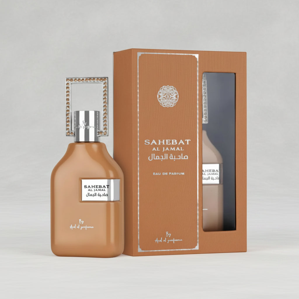 A bottle of Sahebat Al Jamal Eau De Parfum next to its textured brown packaging box, both featuring silver lettering and a silver decorative cap frame, set against a plain light gray background.