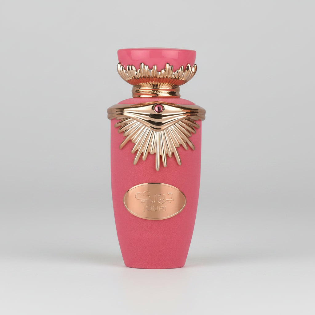 A pink perfume bottle with ornate gold-tone detailing, including a sunburst pattern and a small red gem accent, on a plain white background.
