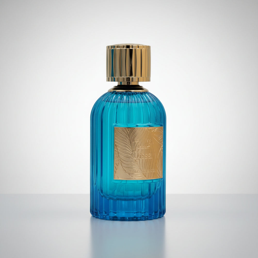 A blue ribbed glass perfume bottle with a gold metallic cap and a gold rectangular label featuring an embossed palm leaf design, set against a plain white background.